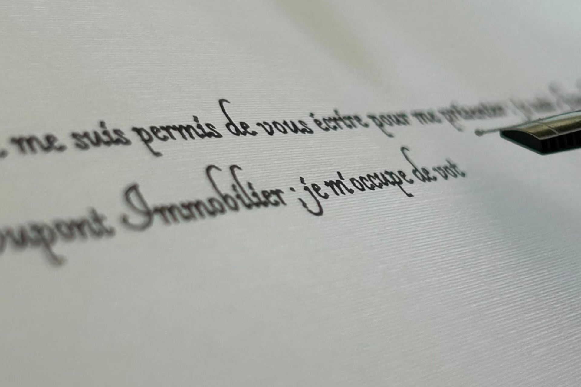 Gros plan sur une plume traçant à l’encre le mot « Immobilier » sur du papier vergé.